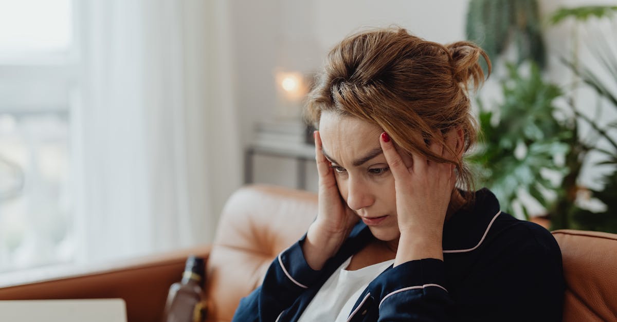 A woman in pajamas sits indoors with hands on head, showing stress and frustration. Perfect for mental health themes.